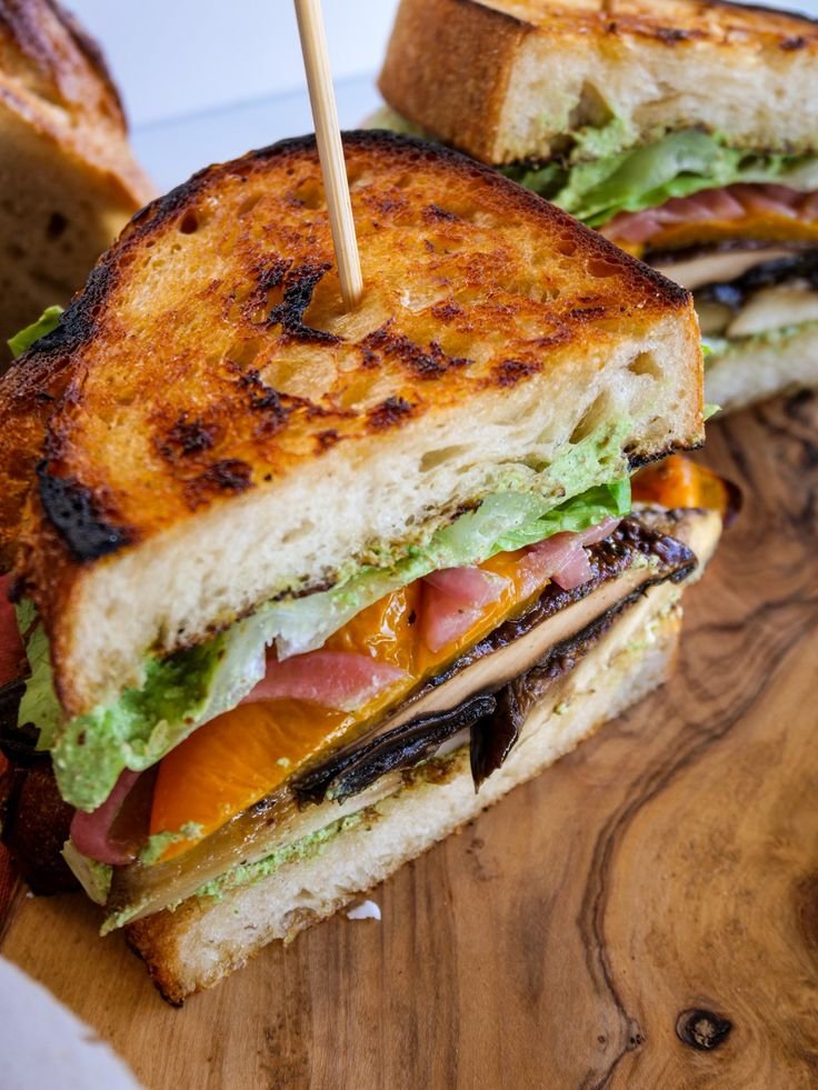 Grilled vegetable sandwich with lettuce on crusty bread, skewered for serving on a wooden board.