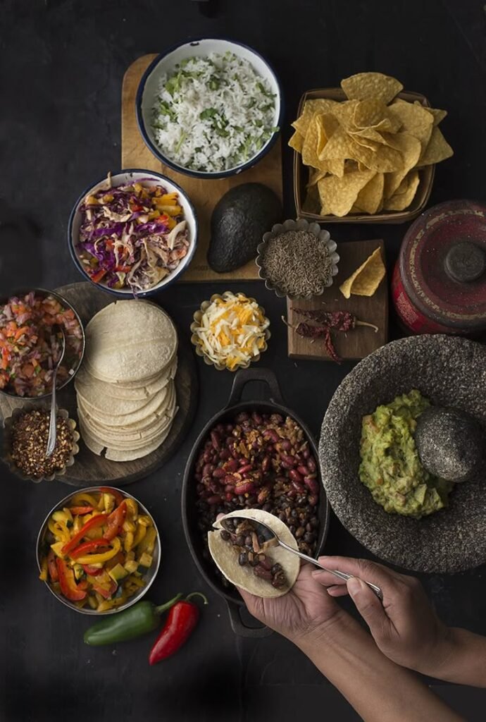 Authentic Mexican feast with tortillas, guacamole, beans, cheese, and toppings arranged on a tabletop.