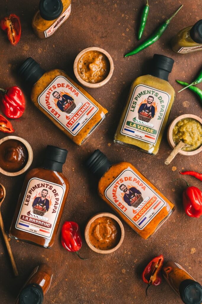 Assorted spicy sauces with fresh peppers, featuring Les Piments de Papa bottles on a rustic brown background.
