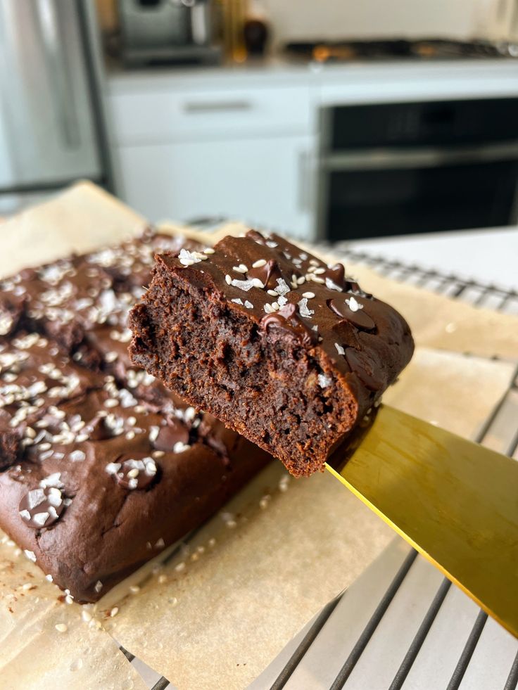 Close-up of a rich, homemade chocolate brownie with a moist texture, garnished with flakes, on a spatula in a modern kitchen.