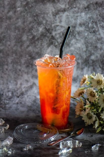 Refreshing iced fruit tea with straw, surrounded by ice cubes and white flowers, against a textured gray background.