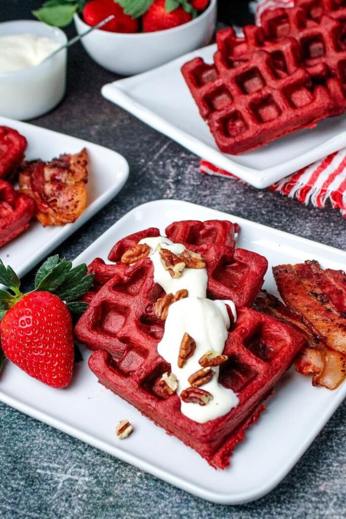 Delicious red velvet waffles topped with cream, pecans, and served with bacon and strawberries. Perfect breakfast treat!