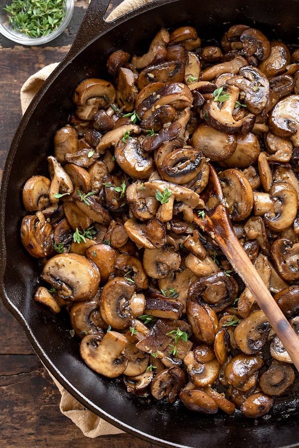 Sautéed mushrooms with herbs in a cast iron skillet, featuring a wooden spoon on a rustic wooden table.