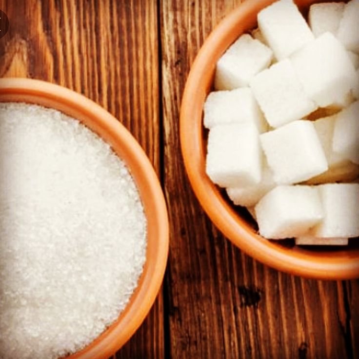 Bowls of granulated sugar and sugar cubes on wooden table, showcasing different forms of sugar for culinary use.