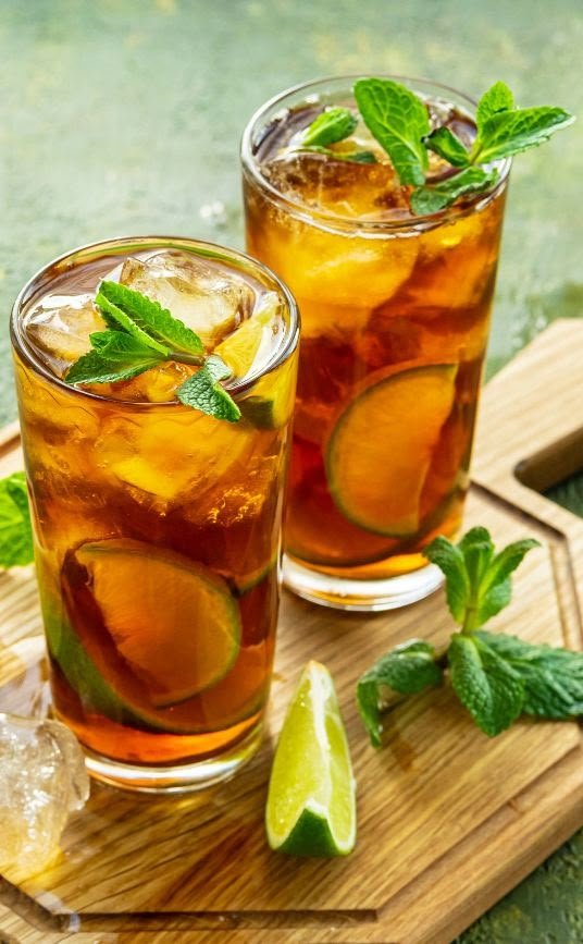 Two refreshing iced teas with lime and mint on a wooden board.