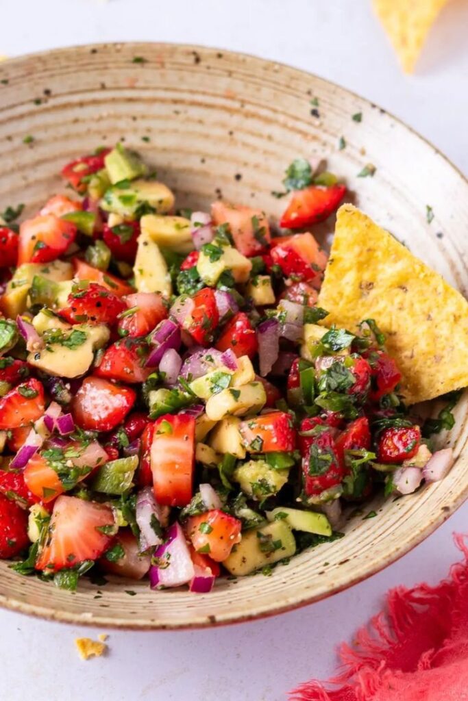 Colorful strawberry avocado salsa in a rustic bowl with a tortilla chip garnish, ideal for summer snacks.