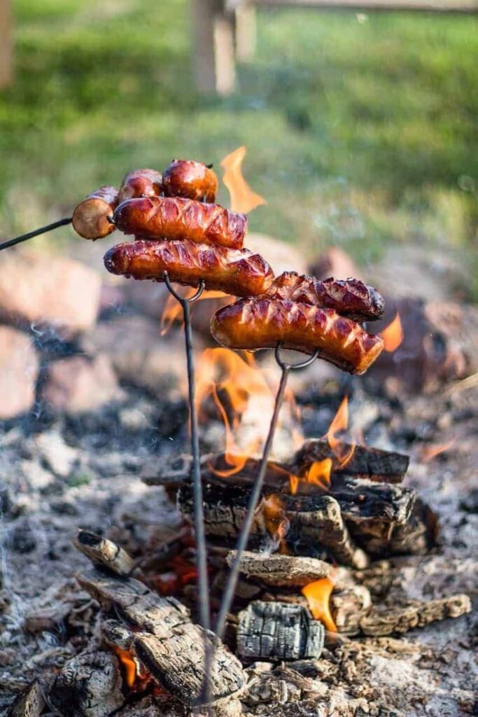 Grilled sausages over an open campfire, sizzling on skewers, outdoor cooking scene.