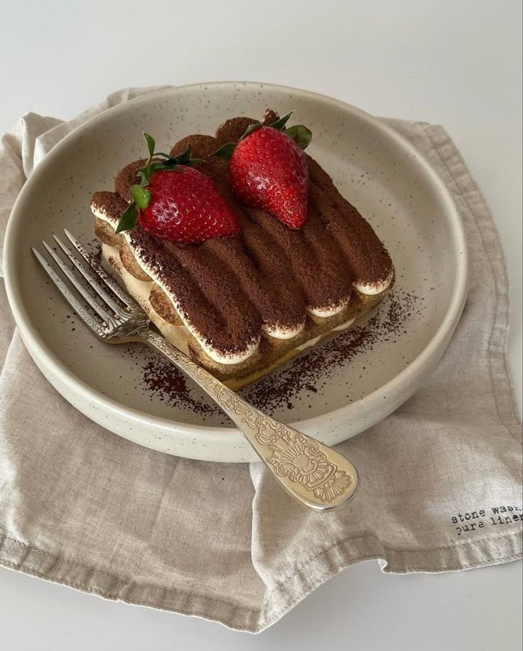 Tiramisu with cocoa and strawberries on a plate, served with a vintage fork on a linen napkin.