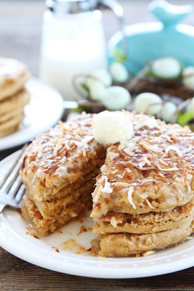 Stack of coconut pancakes with syrup and butter on a plate, perfect for a sweet breakfast treat.