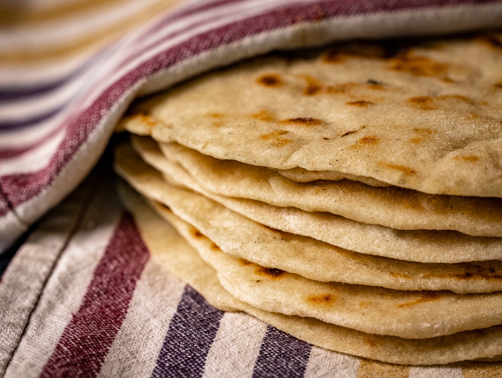 Stack of freshly baked flatbreads wrapped in a striped cloth, showcasing rustic homemade bread.
