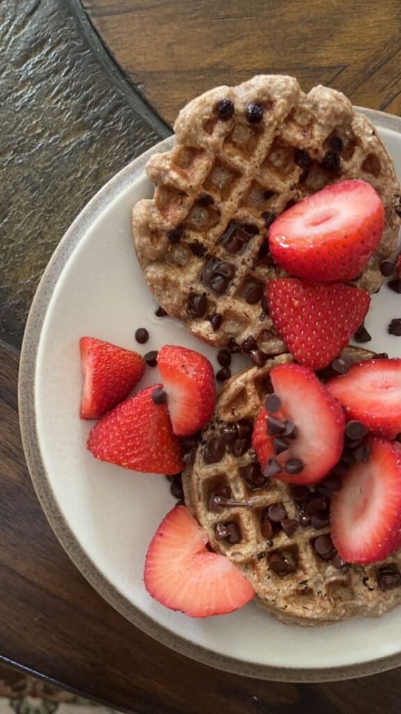 Whole grain waffles topped with fresh sliced strawberries and chocolate chips on a white plate.