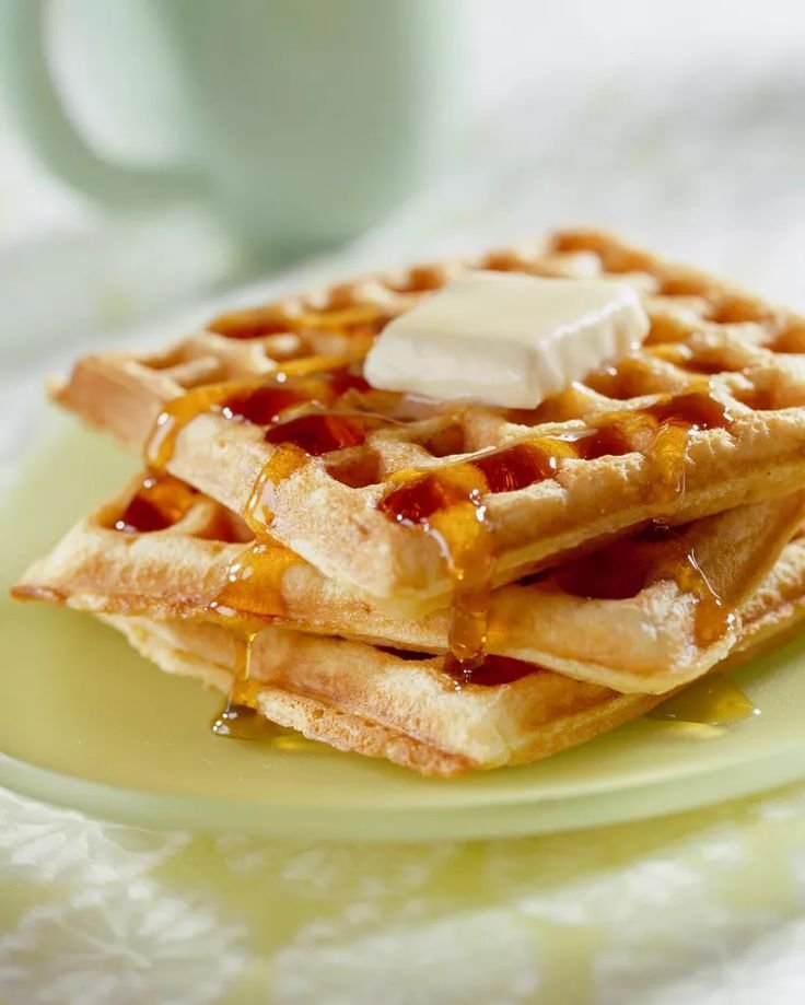 Stack of waffles topped with melting butter and syrup on a plate, close-up breakfast image.