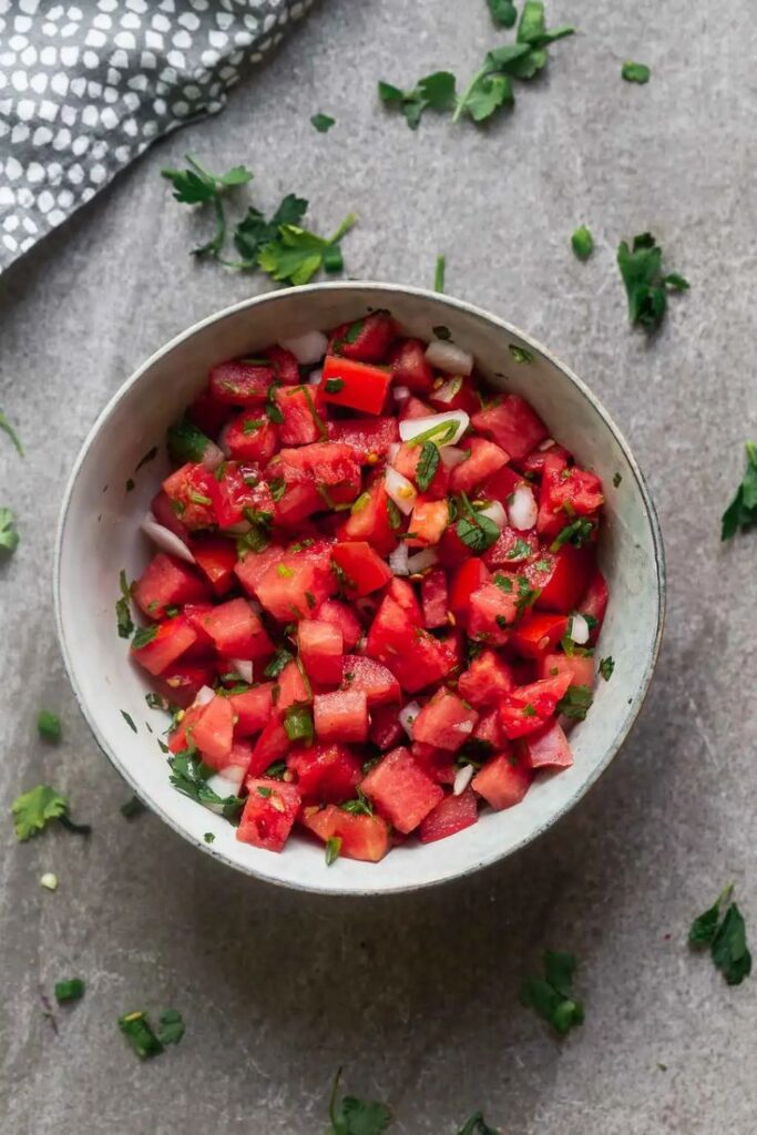 Fresh watermelon salad with chopped herbs in a white bowl on a grey background. Perfect for summer.