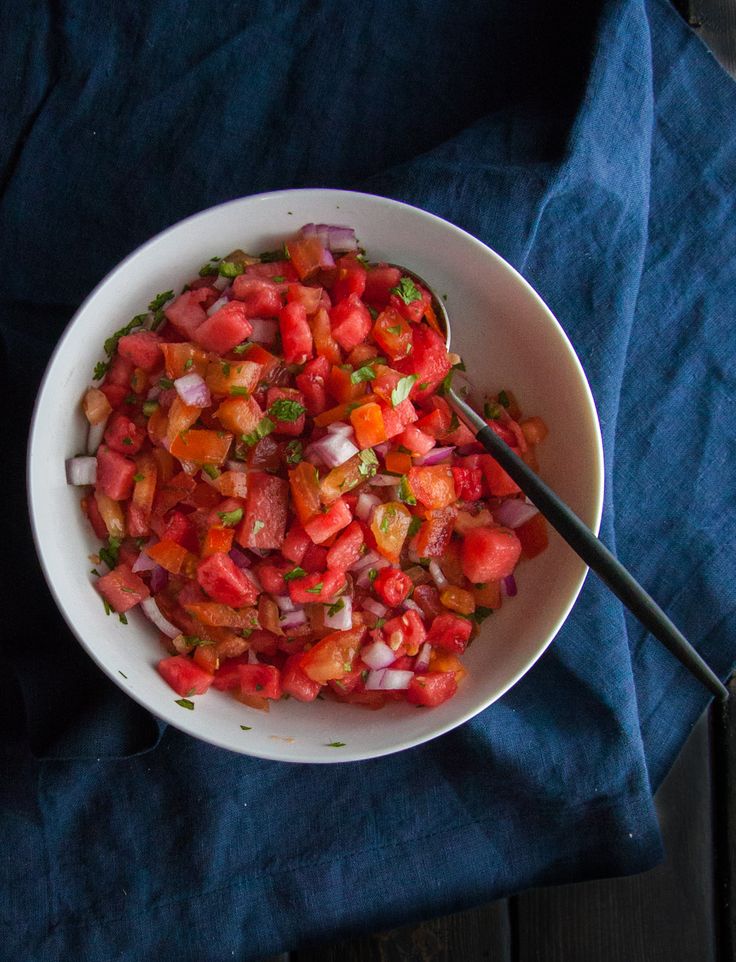 Fresh watermelon salad with peppers, onions, and herbs in a white bowl on a dark tablecloth.