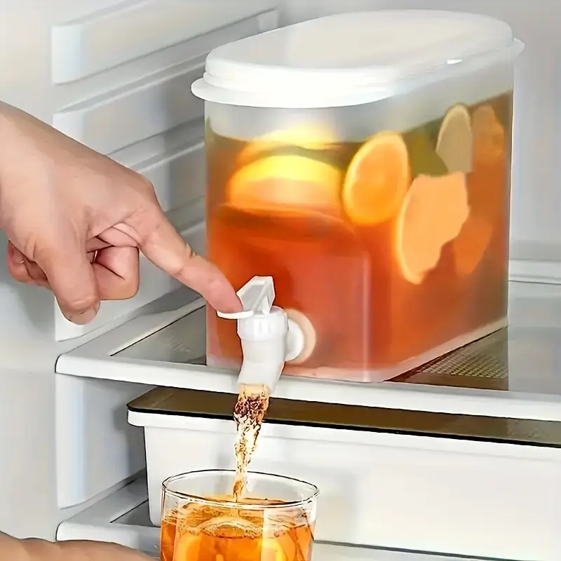 Hand pours citrus iced tea from fridge dispenser into glass.