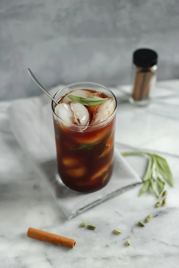 Iced chai latte with cinnamon and herbs on marble surface, perfect refreshing drink.