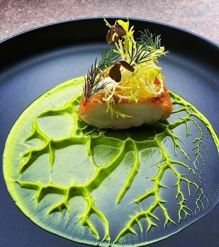 Elegant dish with seared fish, vibrant green sauce, and delicate garnish on a dark plate. Fine dining presentation.