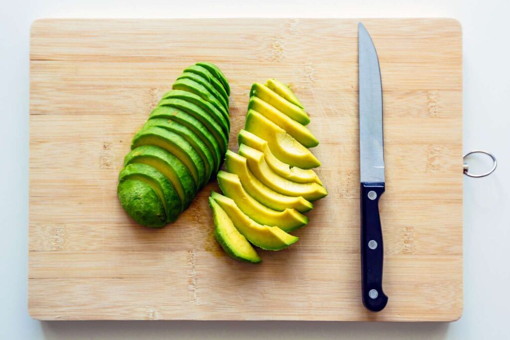 Sliced avocado and knife on a wooden cutting board, ready for a fresh meal preparation.