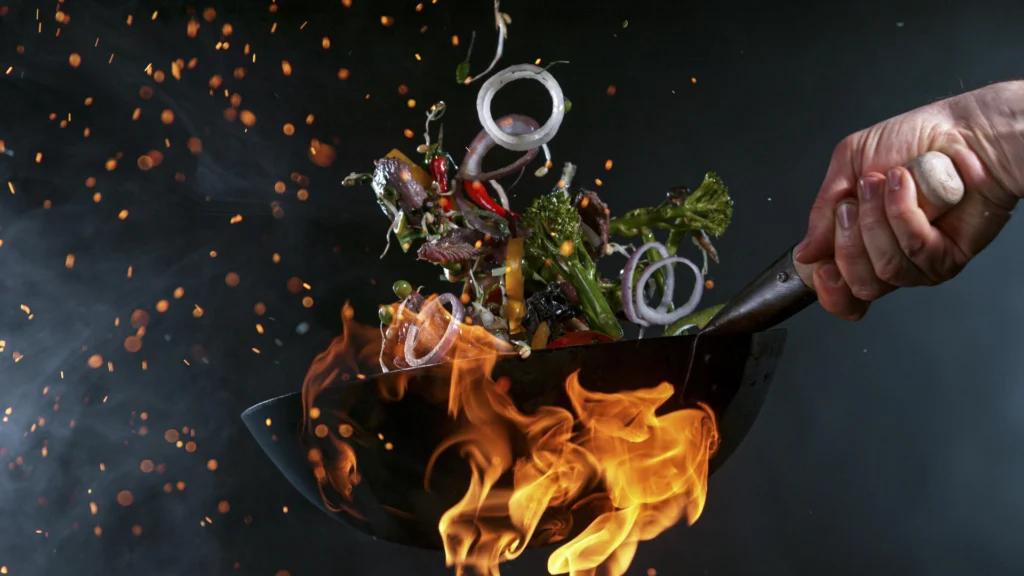 Chef tossing vibrant vegetables in a flaming wok, creating a dynamic culinary scene with vibrant sparks.