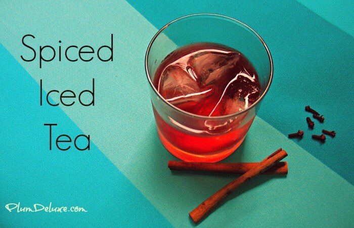 Glass of spiced iced tea with cinnamon sticks and cloves on a blue background. Text: Spiced Iced Tea from PlumDeluxe.com.