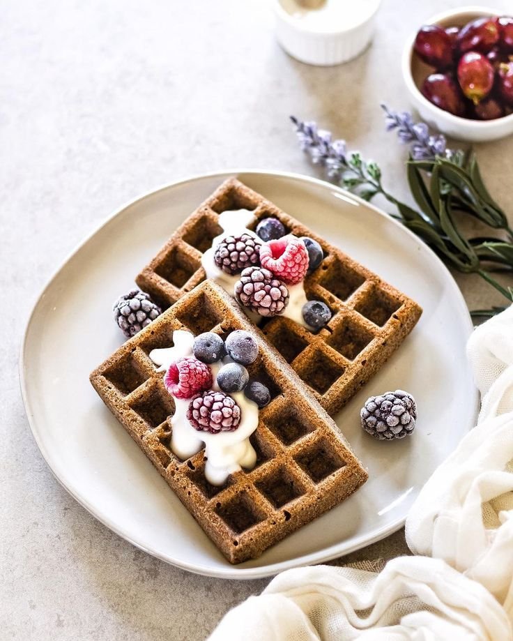 Whole grain waffles topped with yogurt, frozen berries on a plate, garnished with lavender sprigs. Perfect breakfast delight.