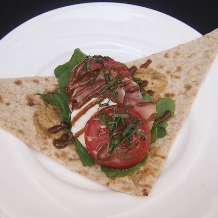 Caprese salad wrap with tomato, mozzarella, basil, and balsamic glaze on flatbread, served on a white plate.