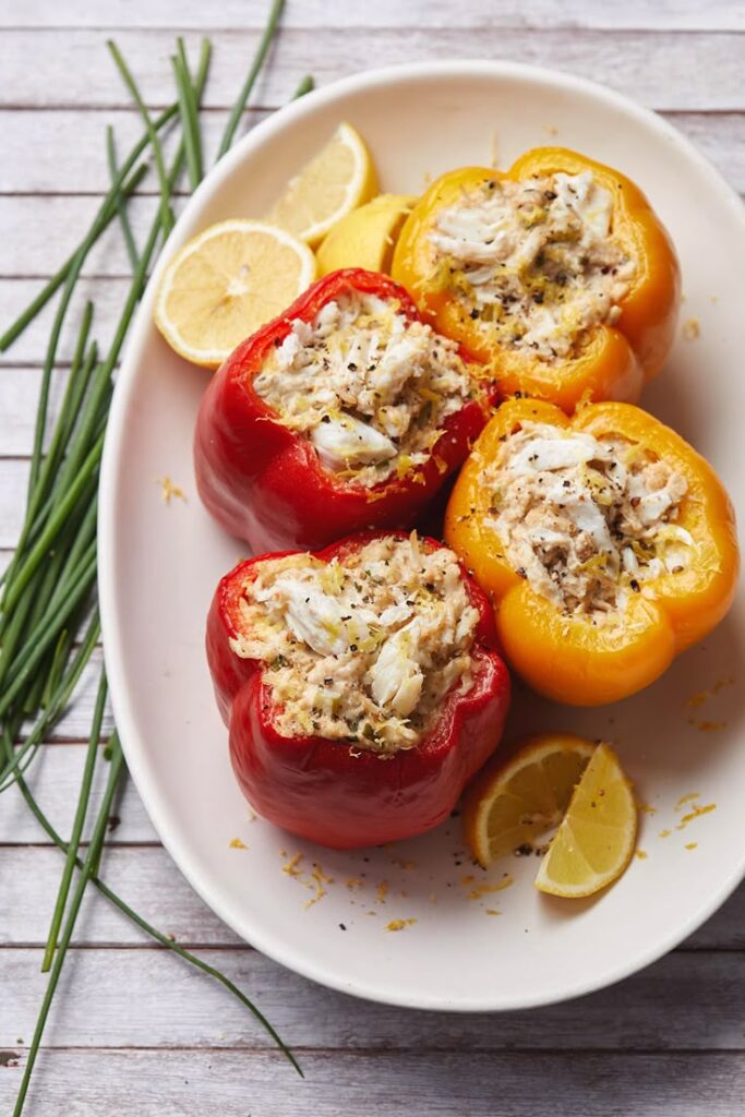 Stuffed bell peppers with crab and lemon garnish on a white plate, perfect for a delicious seafood delight.