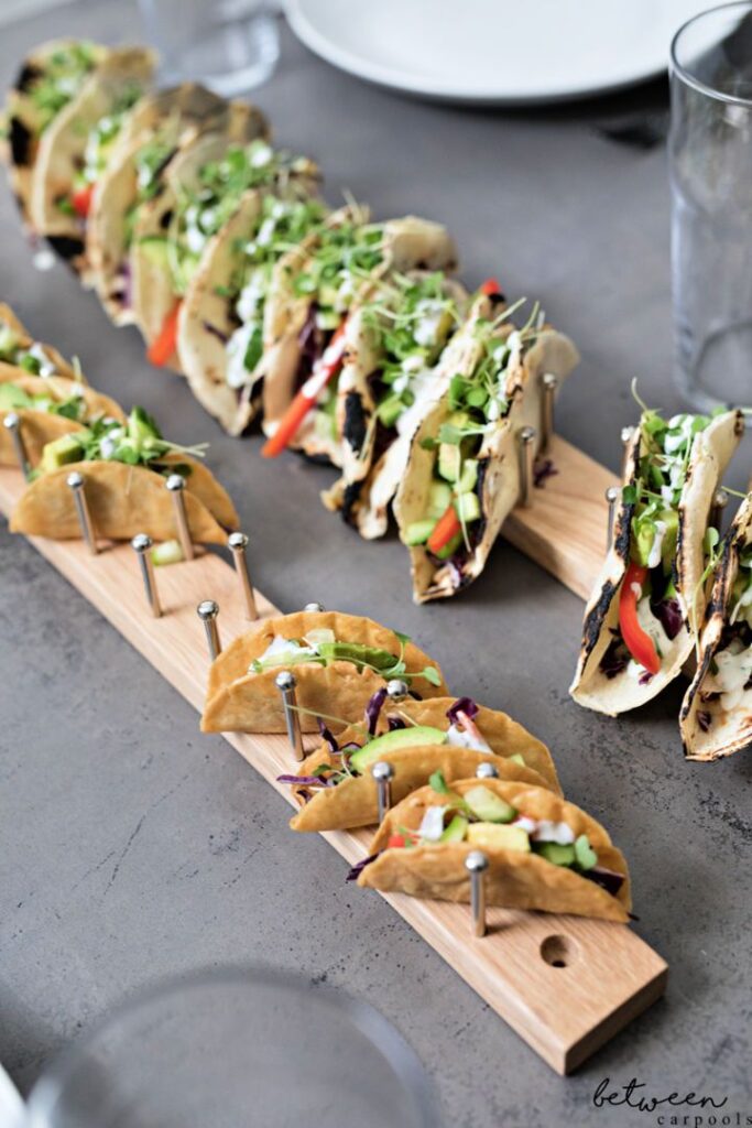 Assorted tacos with fresh toppings on a wooden serving board, ready for a delicious meal.