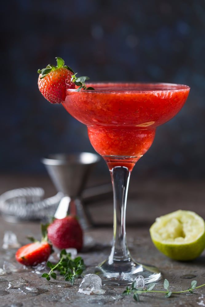 Delicious strawberry cocktail in a glass with fresh fruit and lime garnish, set against a rustic background.