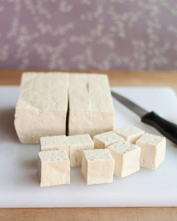 Cubed tofu on cutting board with knife, ready for cooking or recipes.