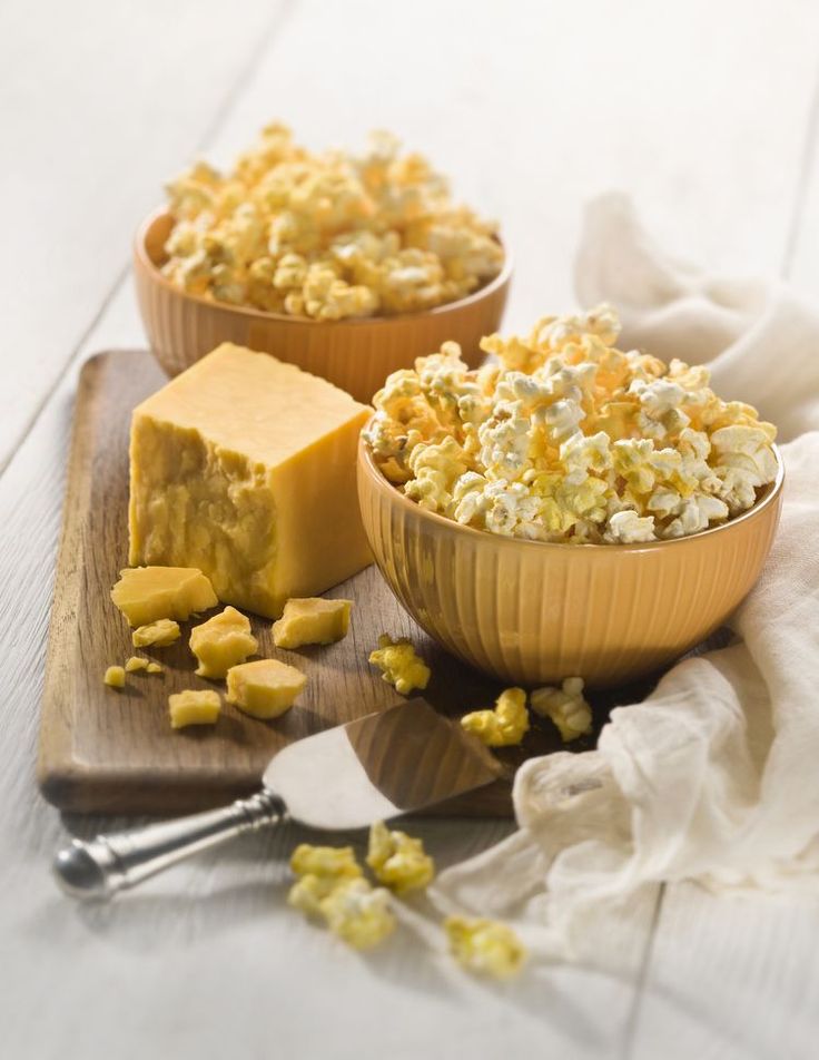 Cheddar cheese and popcorn in bowls on a wooden board, perfect snack for movie nights or casual gatherings.