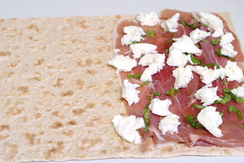Flatbread with prosciutto, fresh mozzarella, and basil, ready to be folded for a delicious wrap.