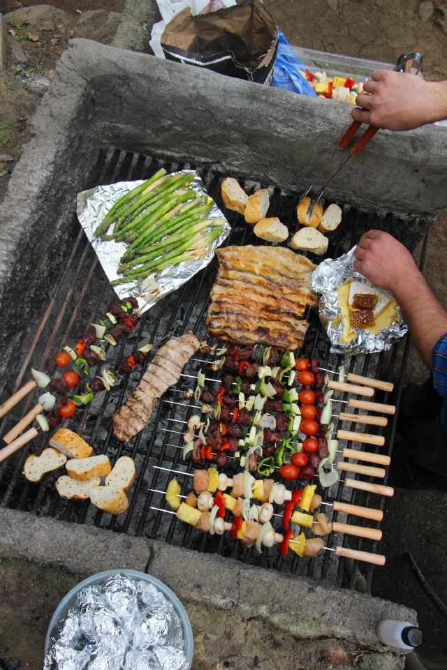 Grilling vegetables, meats, and bread on an outdoor barbecue with skewers and foil-wrapped food.