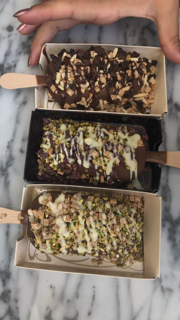 Assorted chocolate ice cream bars with nut toppings and drizzle on a marble surface. Indulgent dessert treat.