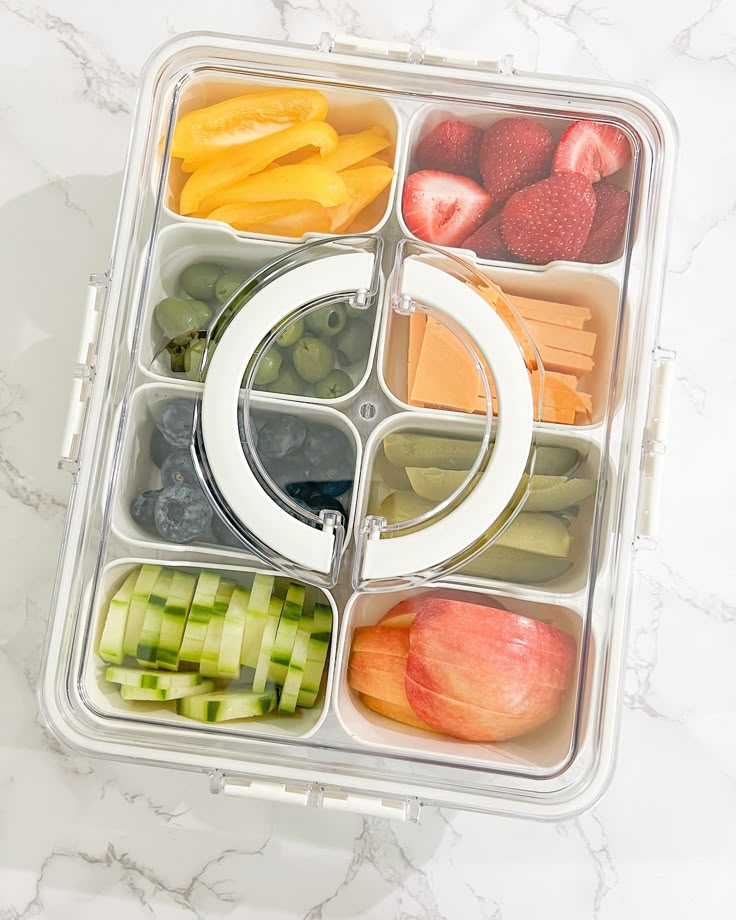 Colorful healthy snacks in a bento box with fruits, vegetables, and cheese on a marble surface.