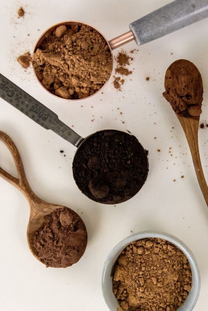Assortment of cocoa powders in scoops and bowls on a white background, ideal for baking or dessert recipes.