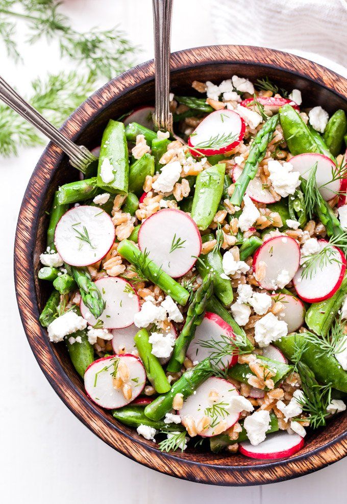 Fresh vegetable salad with radishes, asparagus, peas, quinoa, feta, and dill in a wooden bowl.