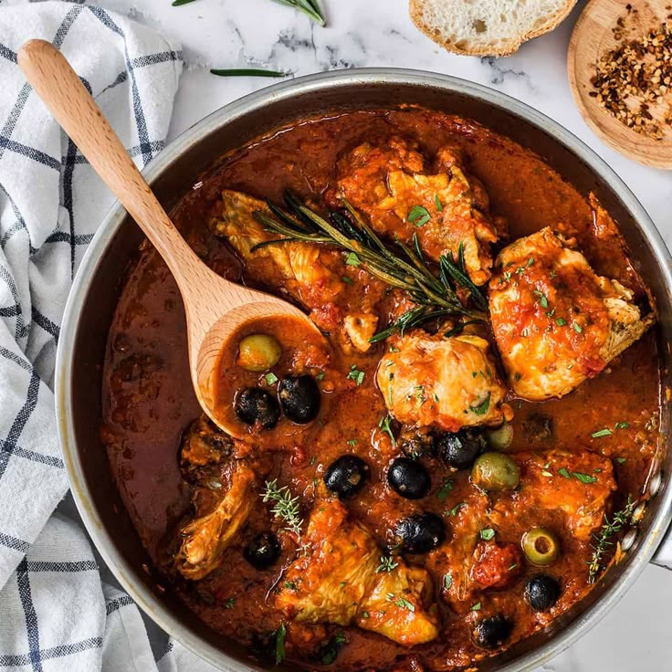 Hearty chicken cacciatore with olives and herbs in a rich tomato sauce, served in a pan with a wooden spoon. Delicious meal.