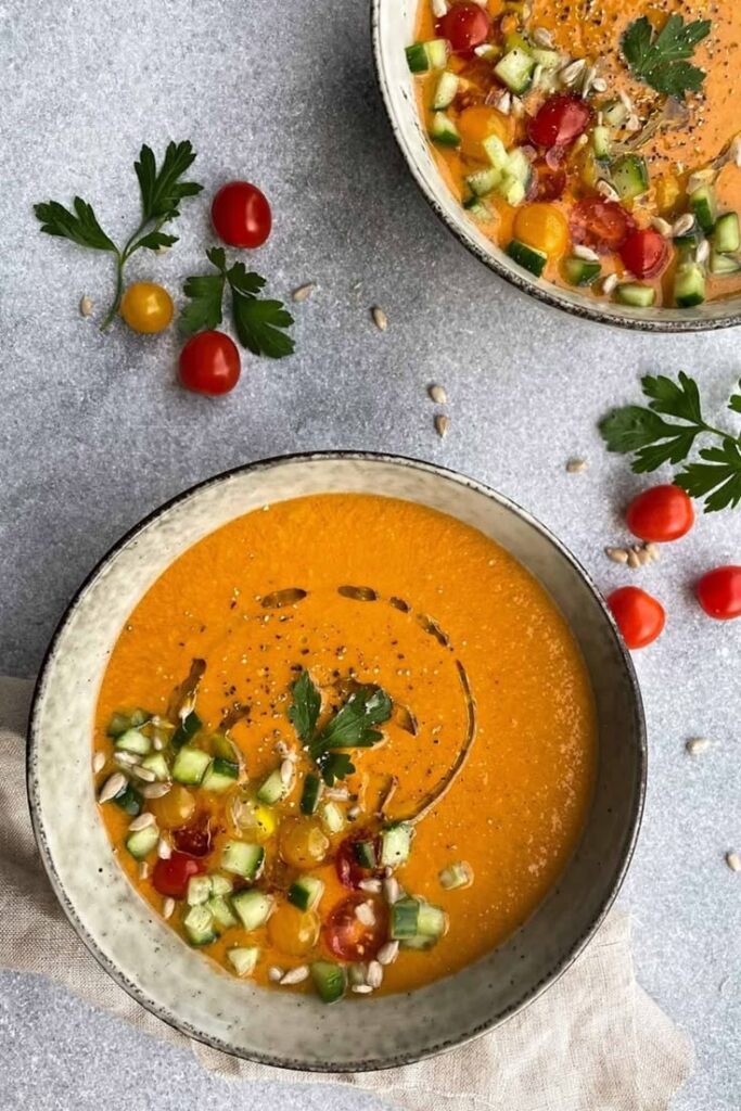 Colorful gazpacho garnished with cherry tomatoes, cucumber, parsley, and seeds in ceramic bowls. Fresh summer dish.