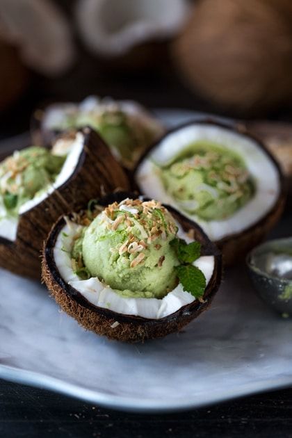 Creamy green ice cream served in coconut shells, garnished with mint and toasted coconut flakes on a marble plate.