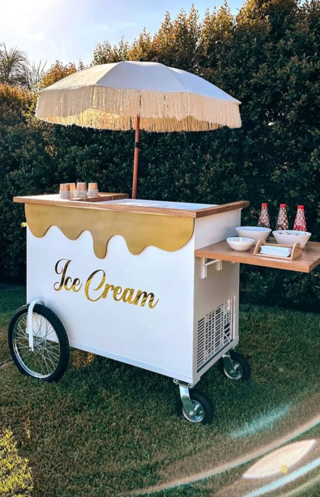 Vintage ice cream cart with umbrella, set up in sunny garden with toppings and cups ready. Retro dessert vibe.