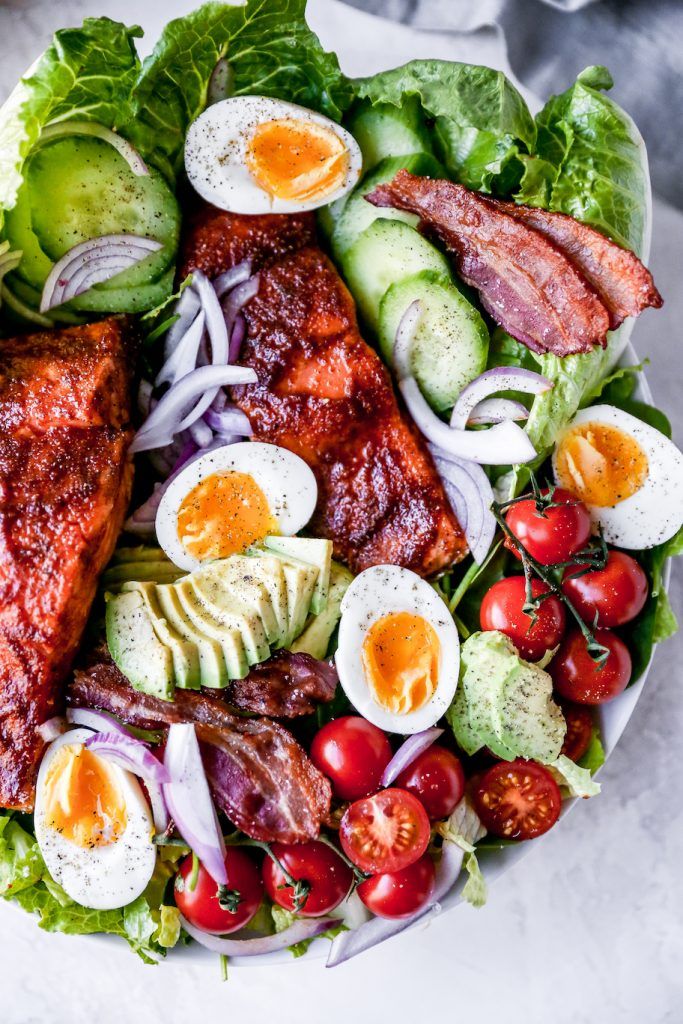 Fresh salad with salmon, avocado, boiled eggs, cherry tomatoes, bacon, and red onion on a bed of romaine lettuce.