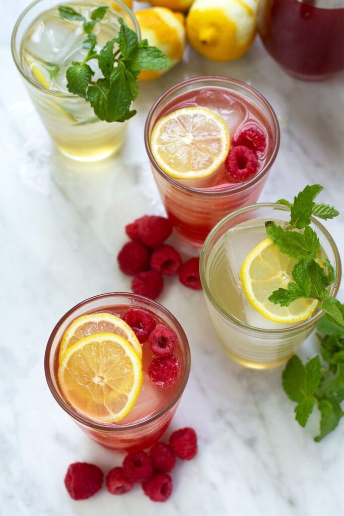 Refreshing raspberry lemonade with mint and lemon slices on ice, surrounded by fresh raspberries and lemons.