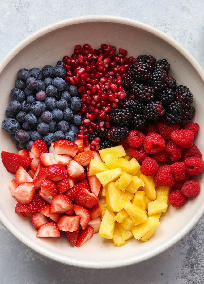 Bowl of fresh mixed fruits: strawberries, blueberries, blackberries, raspberries, pineapple, and pomegranate seeds.