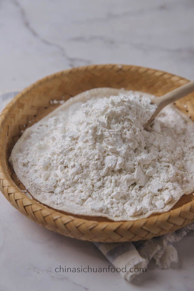 Bamboo basket with a heap of white flour on a marble surface, used in traditional Sichuan cooking recipes.