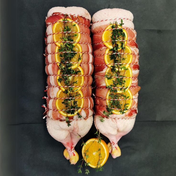 Two stuffed ducks with orange slices and herbs on top, prepared for roasting, on a dark background.