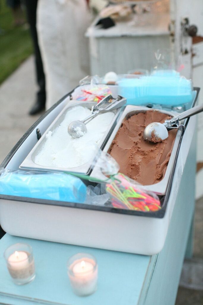 Chocolate and vanilla ice cream in a container with scoops, ready to serve, on a table with candles.