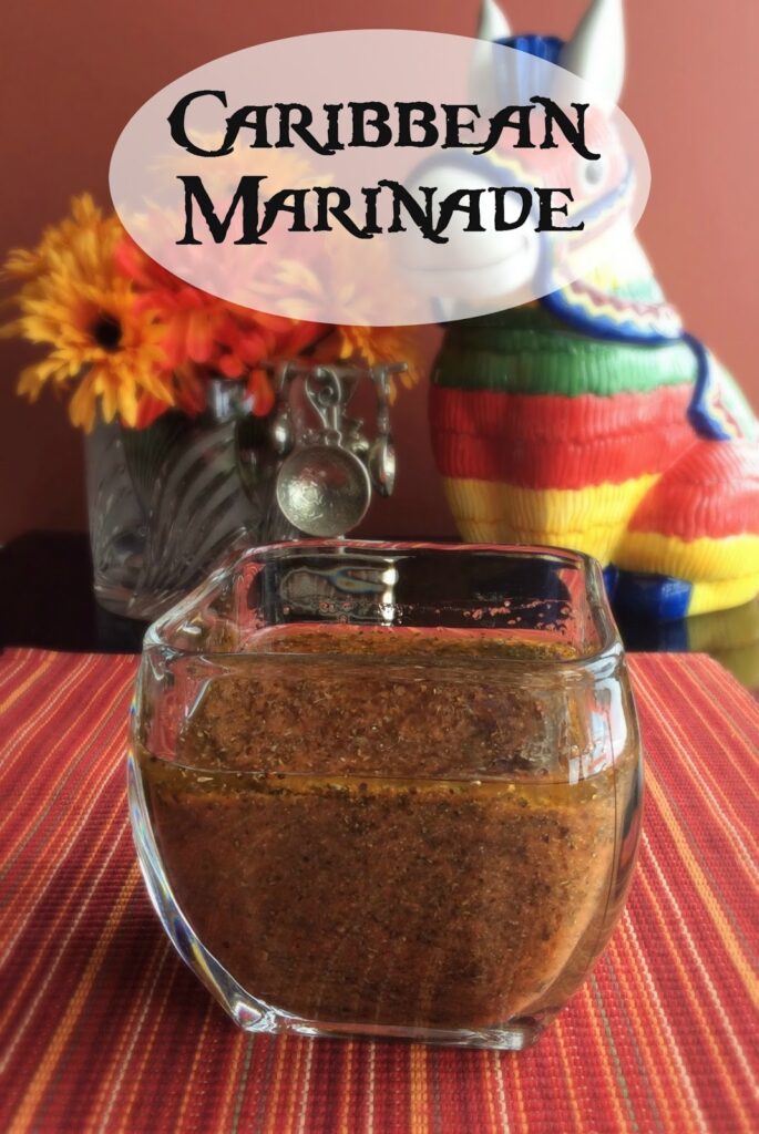 Rustic jar with Caribbean marinade on a vibrant striped tablecloth, bright florals, and a decorative figure.
