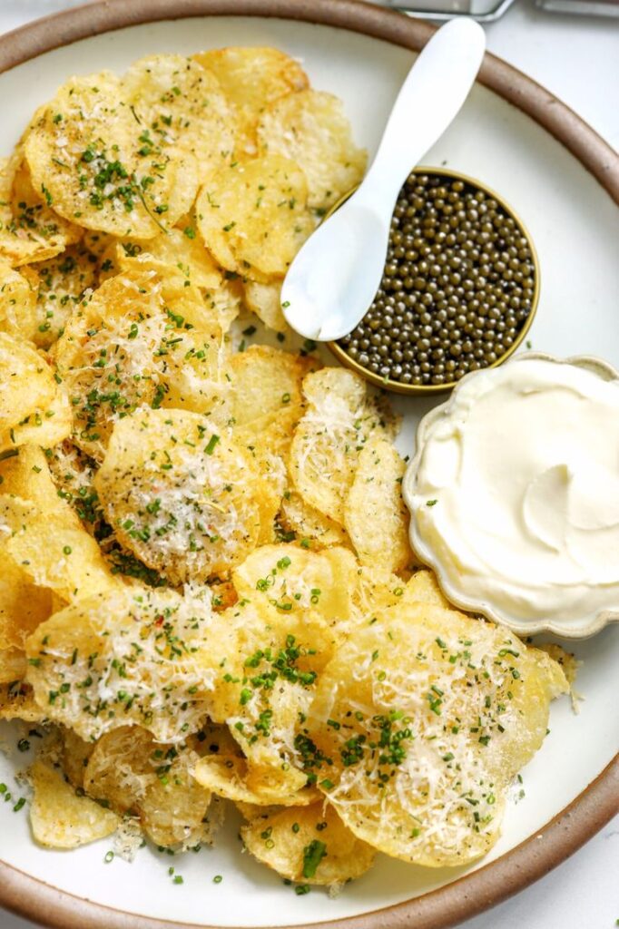 Crispy potato chips with grated cheese, chives, sour cream, and caviar served on a plate with a spoon.
