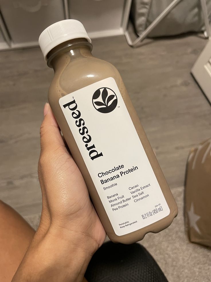 Pressed Chocolate Banana Protein smoothie bottle held in hand, highlighting ingredients like almond butter and pea protein.